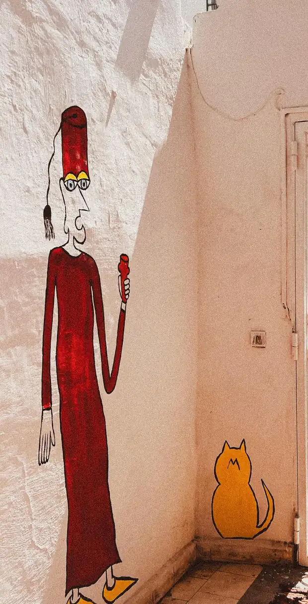 Dans un angle de mur à la chaux, un personnage longiligne en djellaba rouge, tarbouche et babouches jaunes, peint au trait noir&nbsp;; à ses pieds, un chat jaune assis, peint lui aussi.