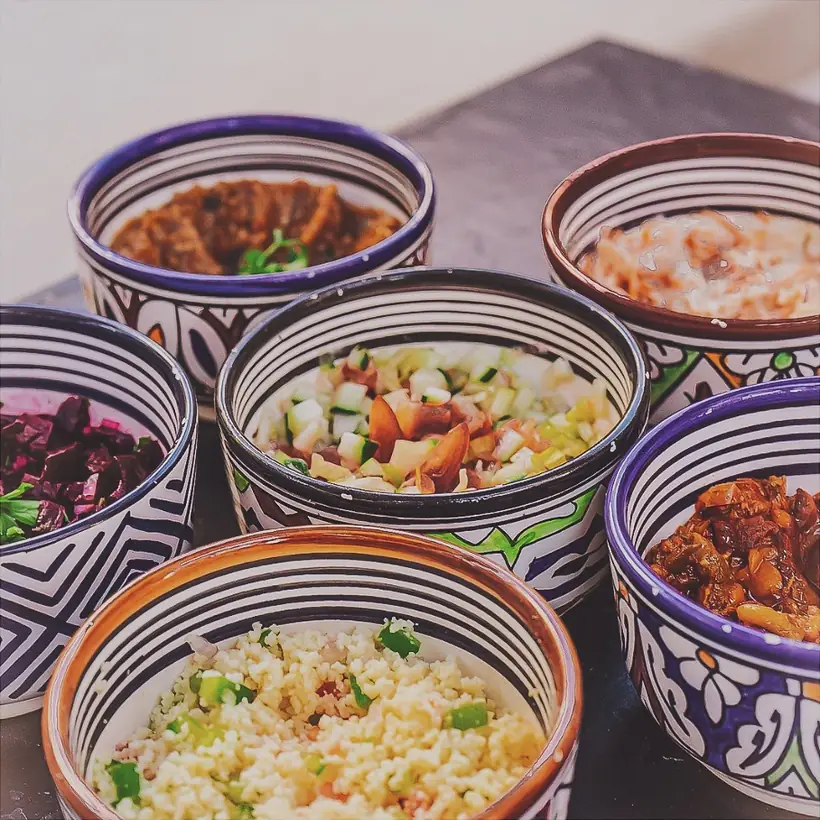 Six bols de céramique de Fès à motifs noirs et bleus, remplis chacun d'une salade différente&nbsp;: aubergine, betterave, taboulé, poivrons confits, salade concombre-tomate.